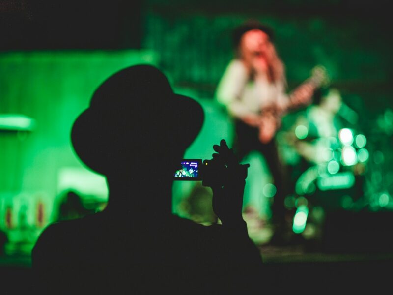 silhouette of man holding camcorder near woman singing on stage